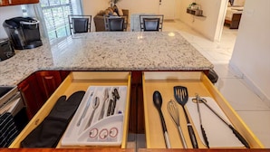 A kitchen with a granite countertop, two drawers with utensils, and a coffee maker.
