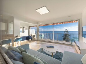 Un moderno salón con sofá, una mesa de centro y vistas al mar a través de amplios ventanales correderas.