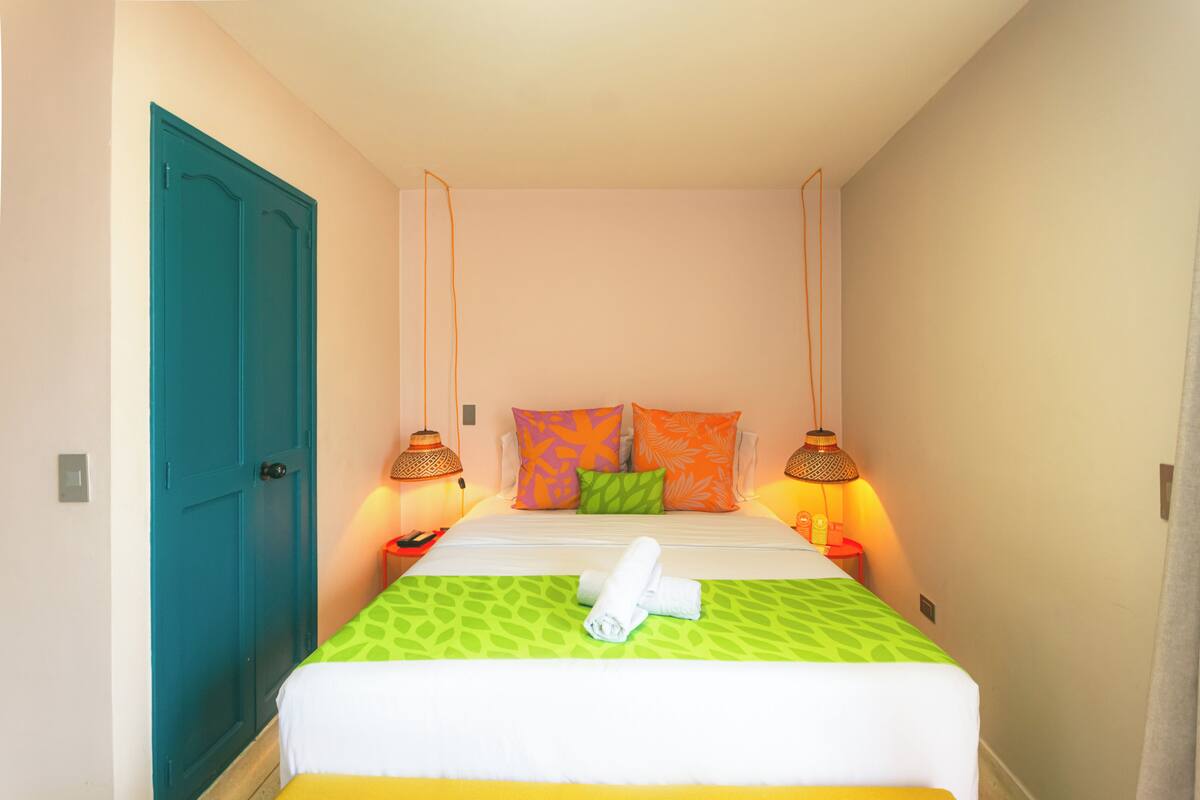 A hotel room with a bed, two bedside lamps, a teal door, and a green patterned bedspread.