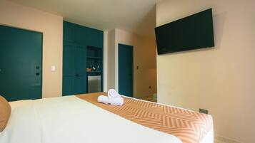 A hotel room with a bed, a TV mounted on the wall, and teal-colored doors.