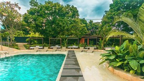 A swimming pool with lounge chairs and a pergola, surrounded by lush greenery. - Del Tropico Hotel (Sopetrán)