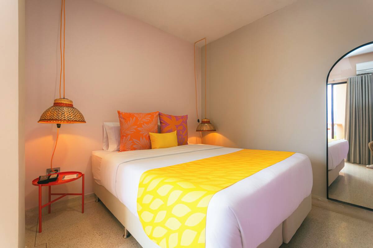 A hotel room with a bed, bedside lamps, a small table, and a mirror.