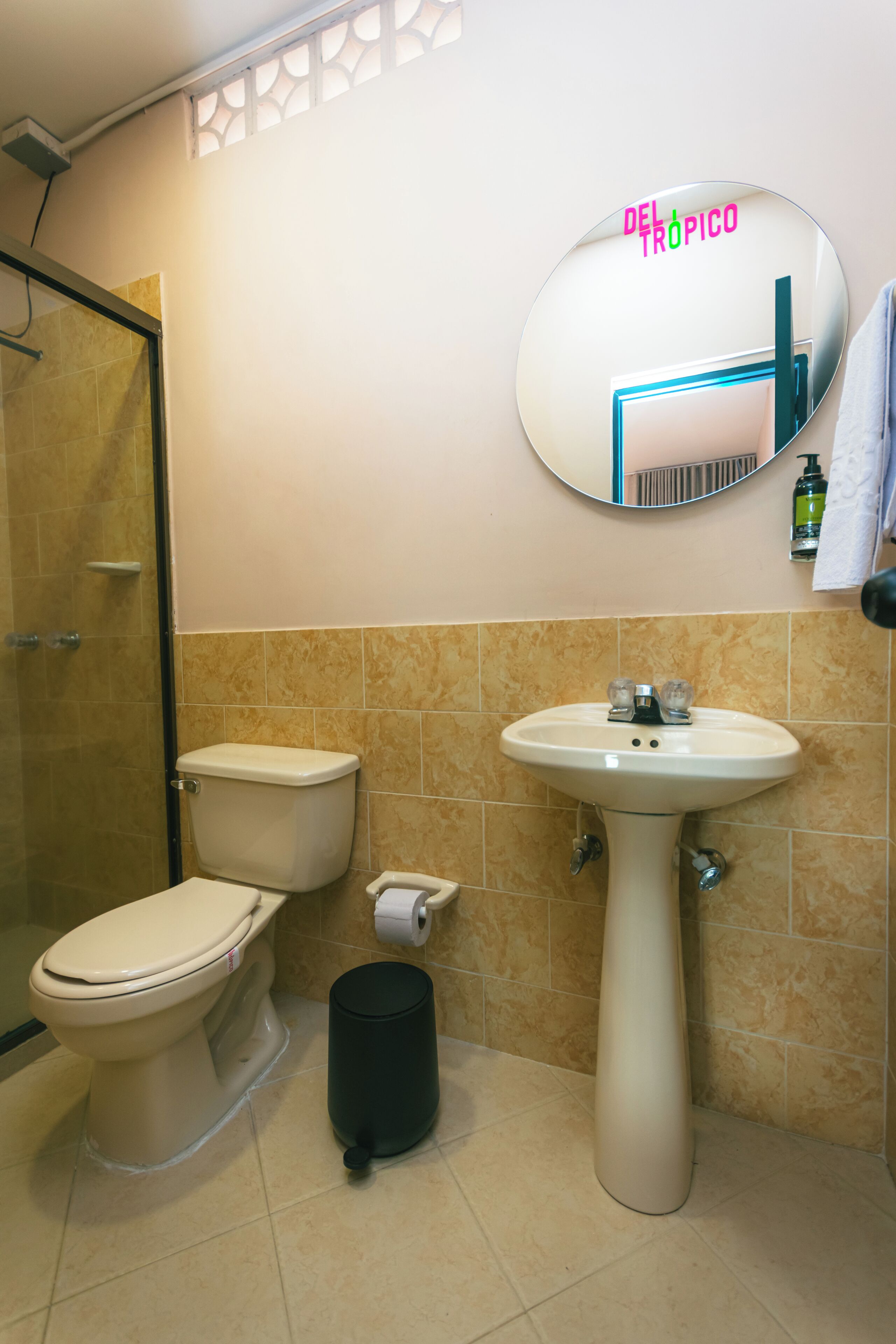 A bathroom with a toilet, sink, and a mirror with 'DEL TROPICO' text.