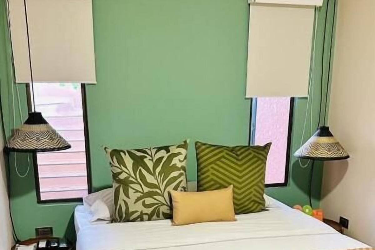 A bedroom with a bed, a bench, two nightstands, and a window with blinds.