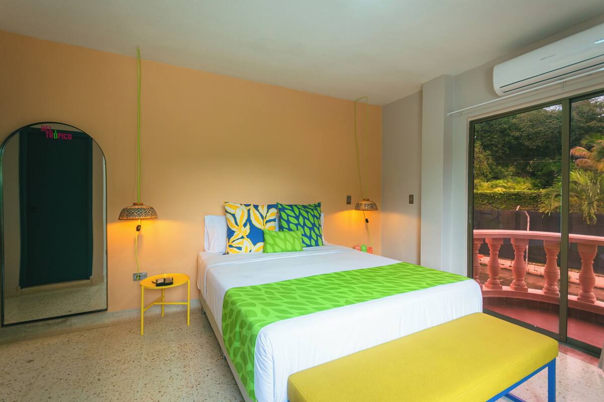 A hotel room with a bed, bedside tables, a mirror, and a balcony with a view.