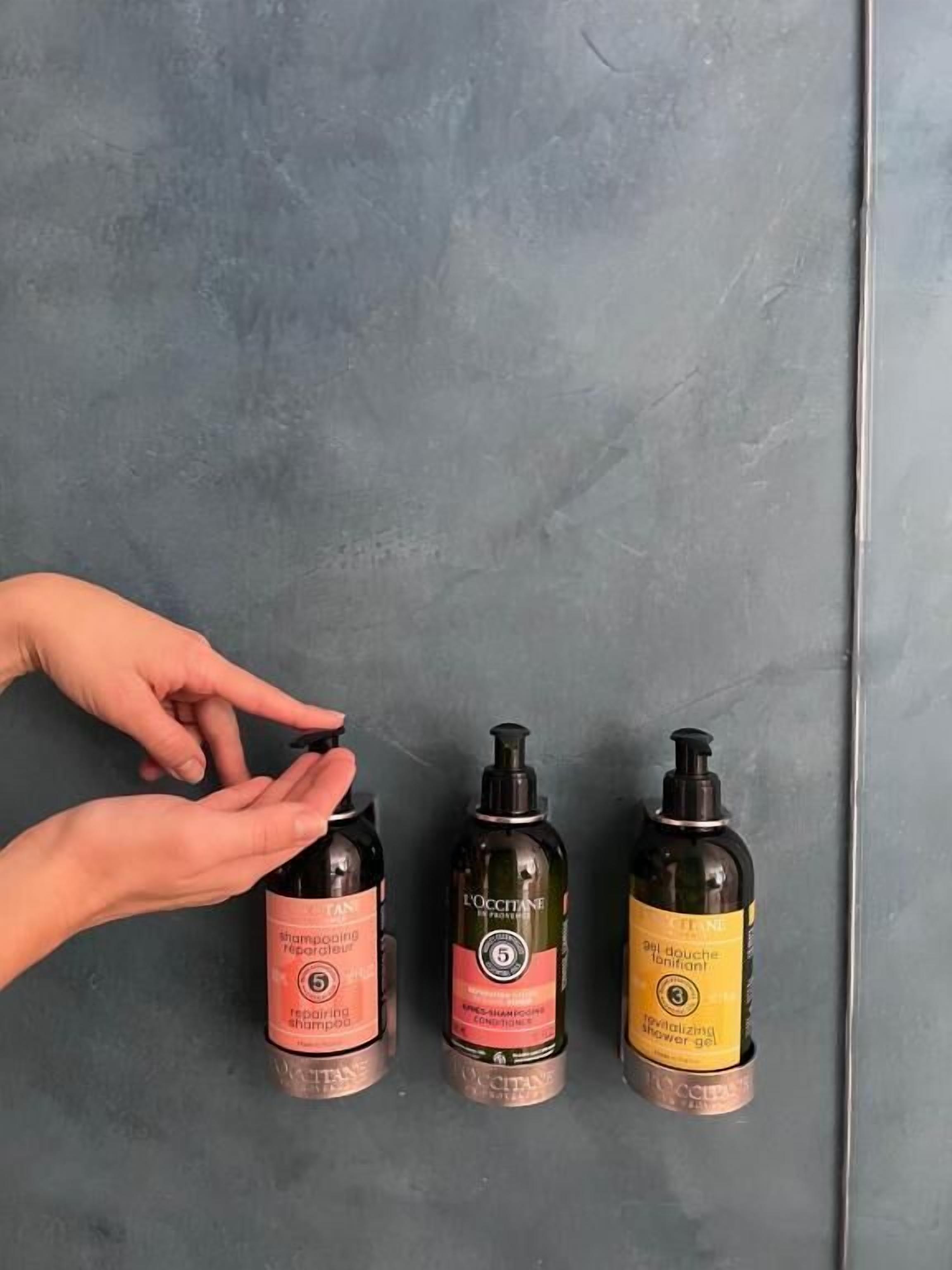 Tres botellas de productos para el cabello de L'OCCITANE sobre una superficie gris con textura.