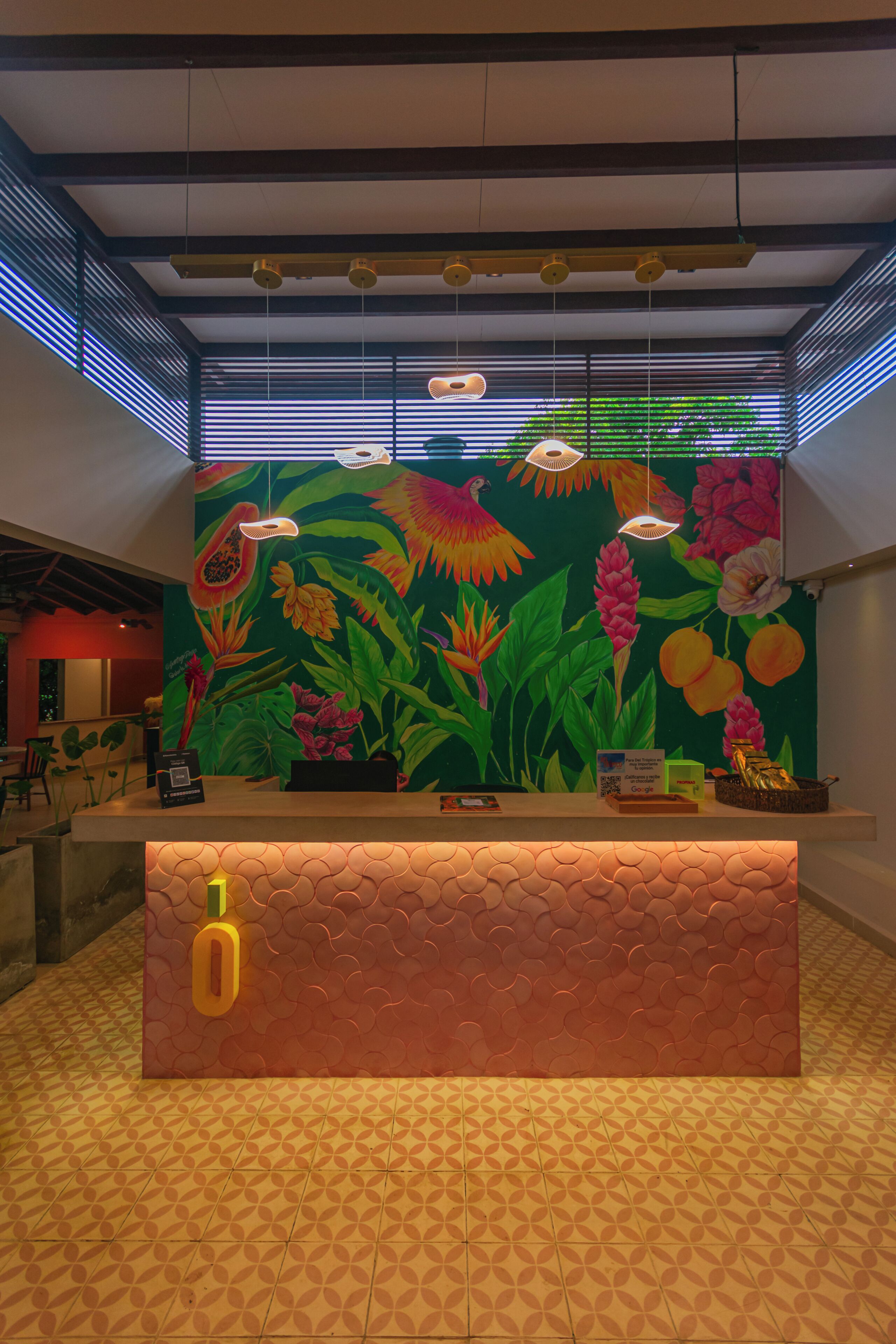 A reception desk with a tropical mural, a patterned floor, and a ceiling with exposed beams and lighting fixtures.