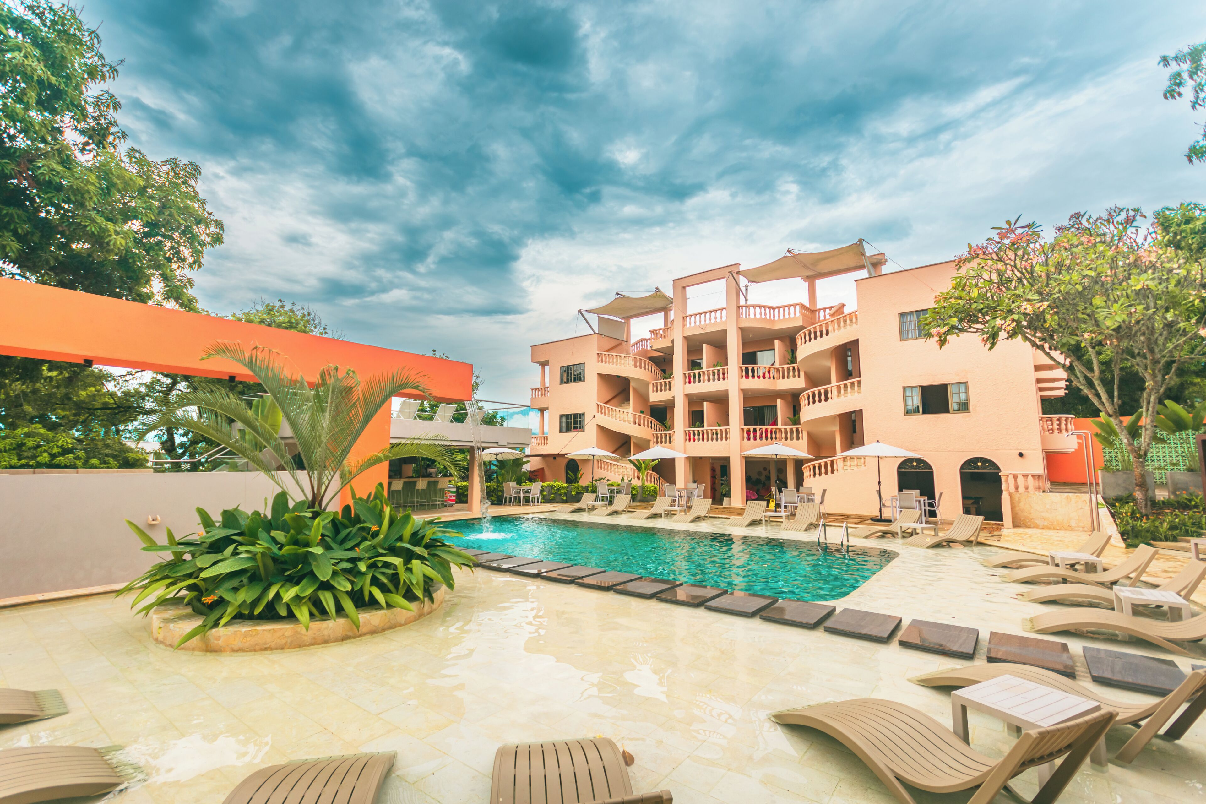 A hotel with a swimming pool, lounge chairs, and a multi-story building with balconies.