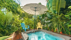A hot tub surrounded by lush greenery, two chairs, and a large umbrella. - Del Tropico Hotel (Sopetrán)