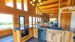 A spacious kitchen with wooden cabinetry, a built-in oven, and a large island with a sink. - Destination Alaska Charters - Cabin 1 (Homer)