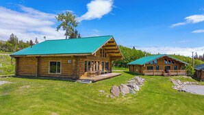 Two log cabins with green roofs, wooden decks, and a grassy yard with rocks. - Destination Alaska Charters - Cabin 1 (Homer)
