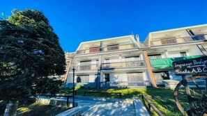 Un immeuble à plusieurs étages doté de balcons, d’une enseigne et d’un grand arbre au premier plan.