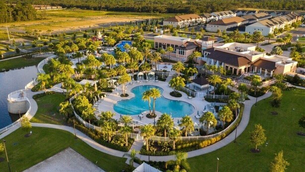 Eine Vogelperspektive zeigt ein Resort mit einem zentral gelegenen Schwimmbad, umgeben von Palmen und verschiedenen Gebäuden.
