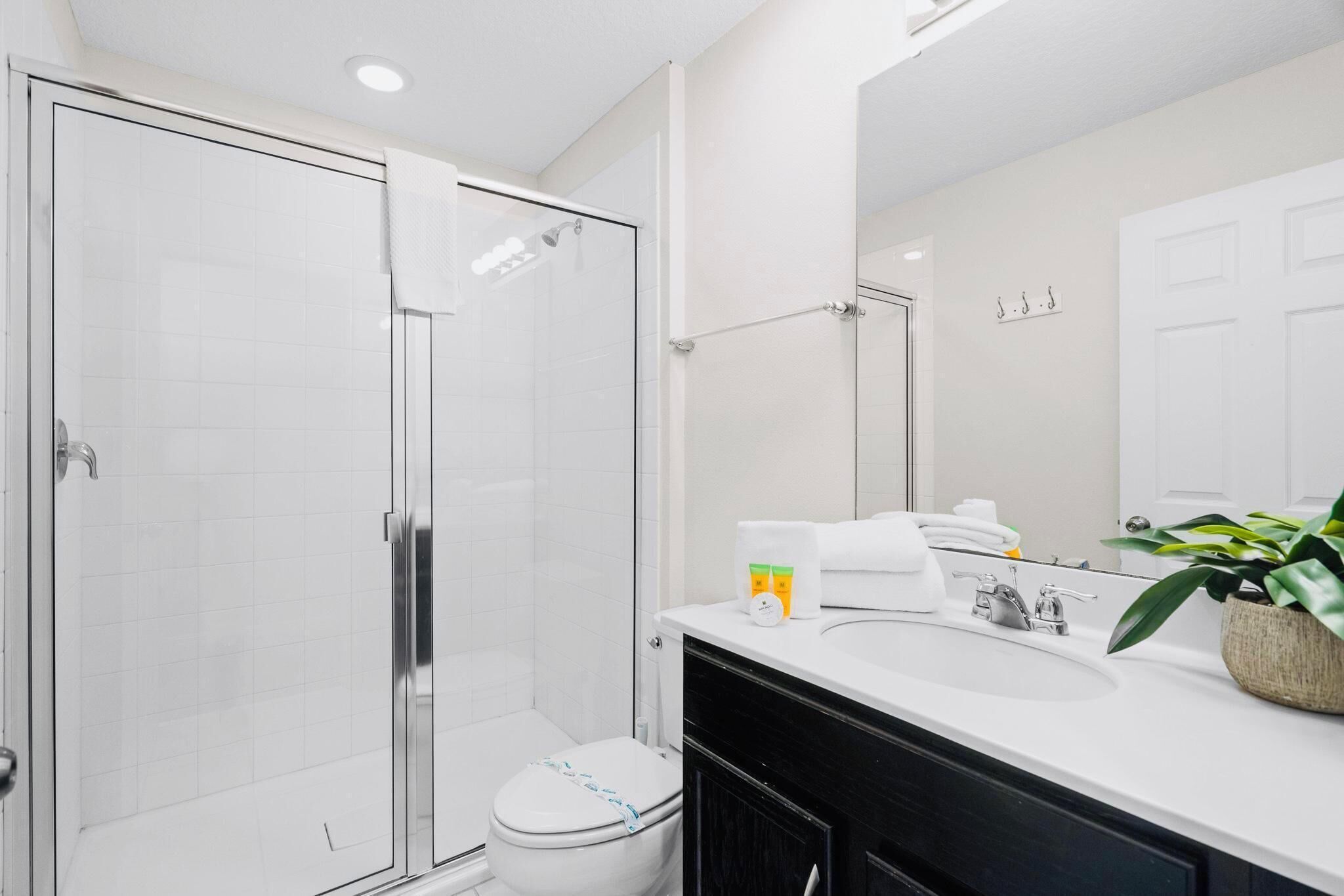 Un bagno moderno con box doccia in vetro, un water bianco e un lavandino con specchio sopra.