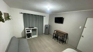 Quarto pequeno e limpo, com uma cama, uma escrivaninha com duas cadeiras, televisão e uma kitchenette compacta.