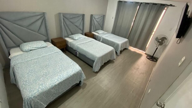 Quarto com três camas, televisão de tela plana e ventilador de teto.