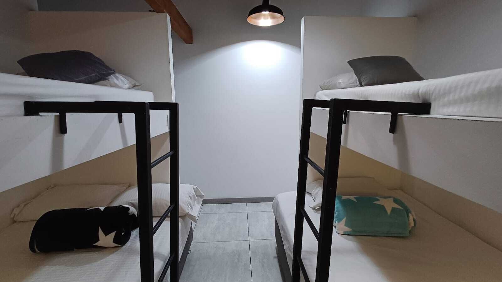 A dormitory room with two bunk beds, a small table, and a ceiling light.
