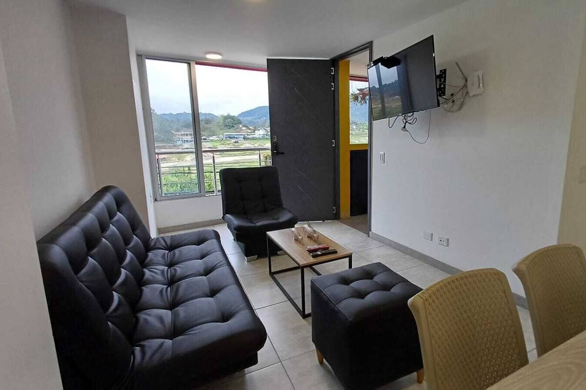 Uma sala de estar moderna com um sofá de couro preto, uma poltrona preta, uma mesa de centro de madeira e uma TV fixada na parede.