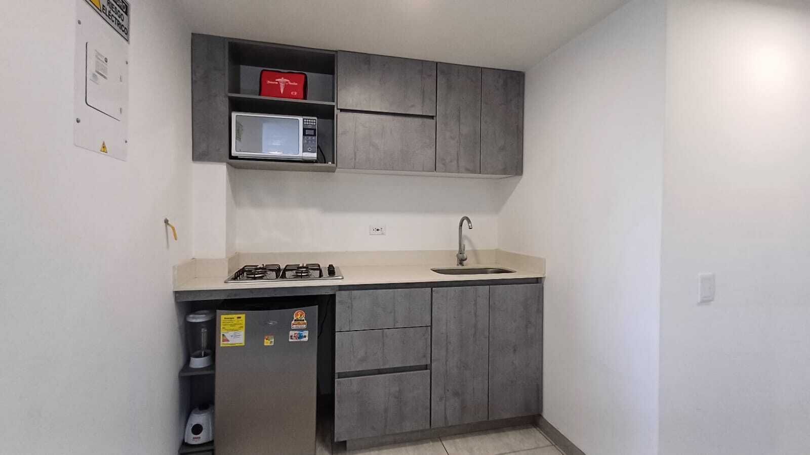 A compact kitchen with a gas stove, a microwave, a sink, and a refrigerator.