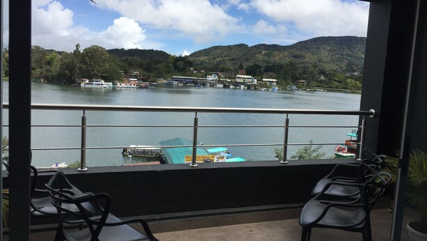 A balcony with two chairs, a view of a lake, boats, and a hilly landscape. - Escape (Guatapé)