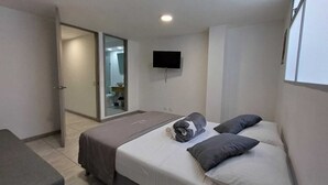 A bedroom with a bed, pillows, a flat-screen TV, and a sliding door leading to a bathroom. - Escape (Guatapé)