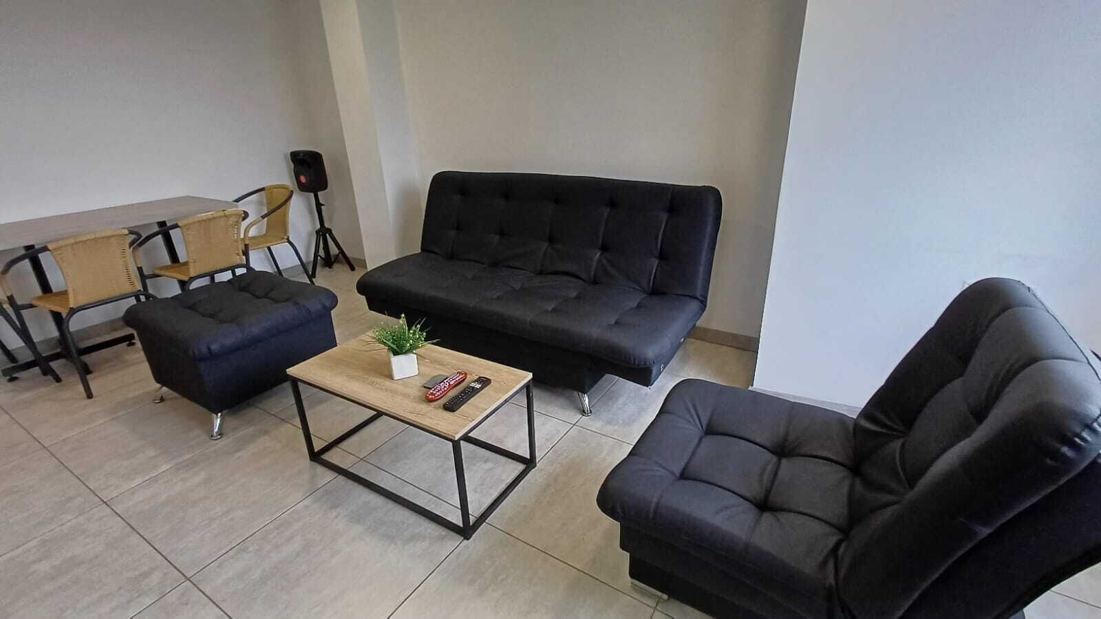 Un salon avec un canapé noir, un fauteuil noir, une table basse en bois et une petite plante.
