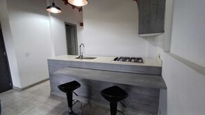 A modern kitchen with a countertop sink, gas stove, and two black bar stools. - Escape (Guatapé)
