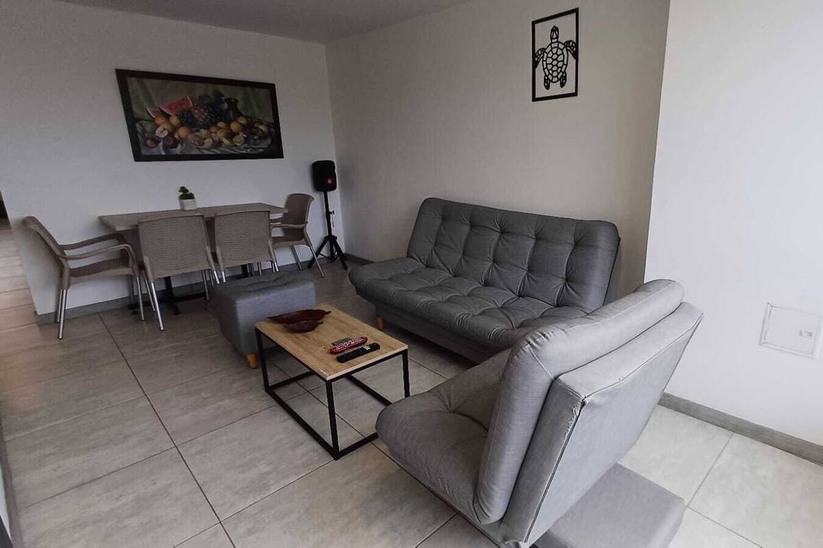 Uma sala de estar com um sofá cinza, uma mesa de centro e um espaço de jantar com cadeiras e mesa.