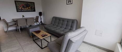 A living room with a grey sofa, a coffee table, and a dining area with chairs and a table.