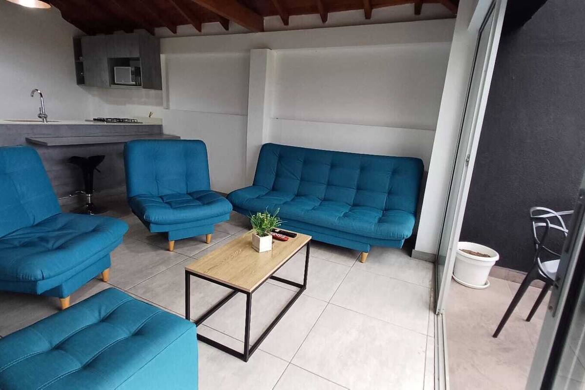 Uma sala de estar moderna com sofás azuis, uma mesa de centro de madeira e uma cozinha ao fundo.