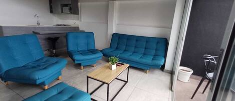 A modern living room with blue sofas, a wooden coffee table, and a kitchen area in the background.
