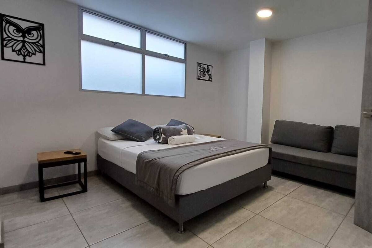 Quarto moderno com cama, mesa pequena, sofá e obras de arte nas paredes.