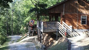 Une cabane rustique avec une façade en bois, une véranda dotée d’une balustrade et un escalier menant à une terrasse.