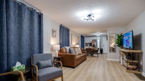 A living room with a brown sofa, a grey armchair, and a wooden coffee table. There is a television on a wooden stand and a plant on the right side. - Pet-Friendly 3BR Dayton Bungalow Near UD (Dayton)