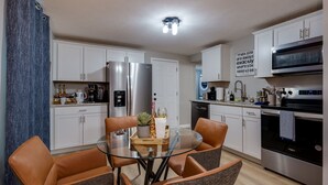 A modern kitchen with white cabinets, stainless steel appliances, and a glass dining table with brown chairs. - Pet-Friendly 3BR Dayton Bungalow Near UD (Dayton)