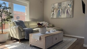 Een woonkamer met een bank, een bijzettafeltje, een potplant en een schilderij aan de muur.