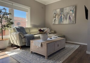 A living room with a sofa, a coffee table, a potted plant, and a painting on the wall.