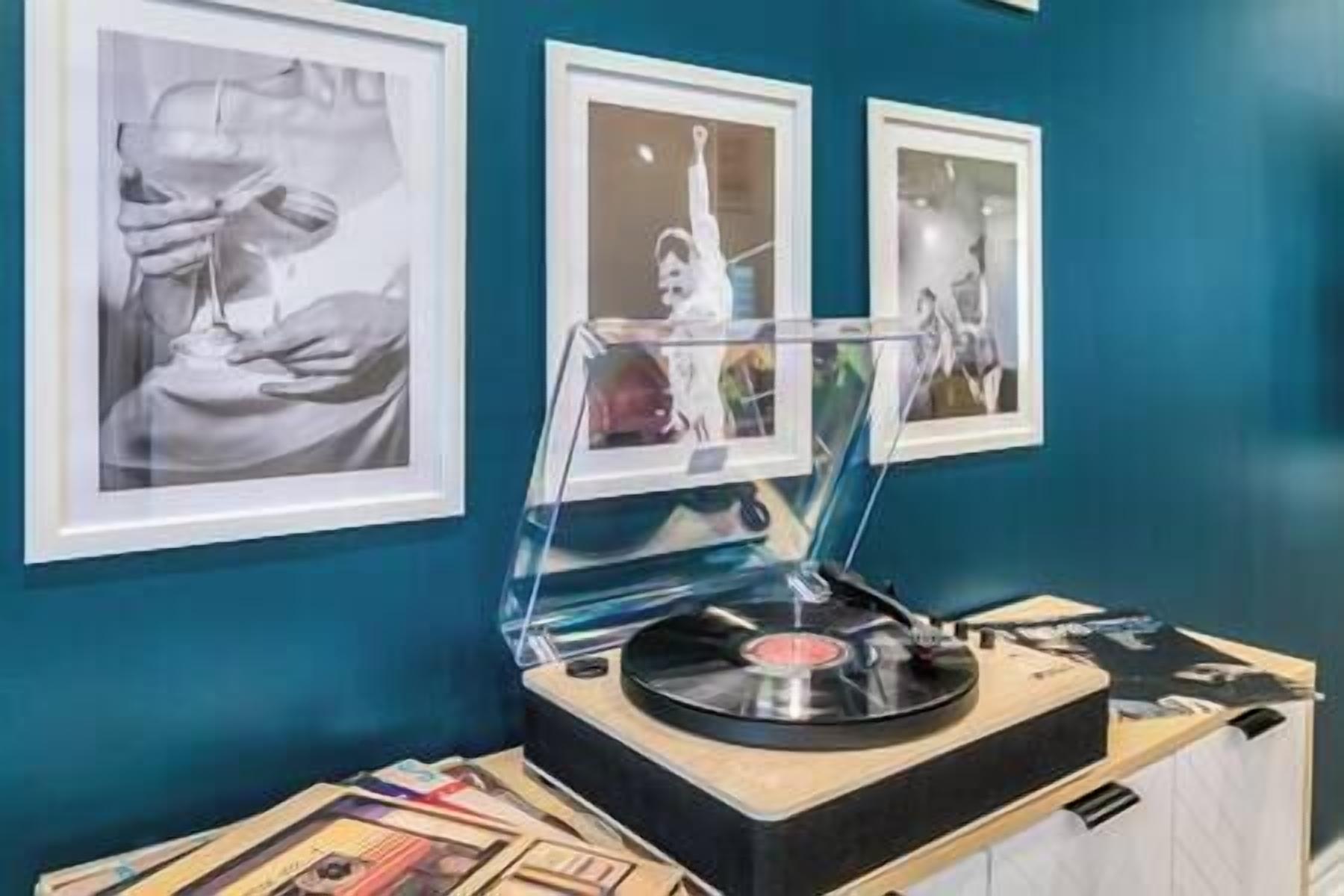 A room with a teal wall, a turntable, and framed black and white photographs.