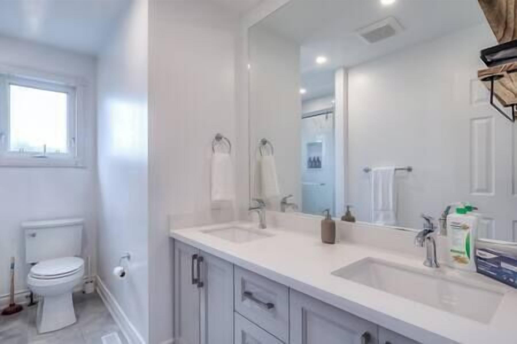 Une salle de bain moderne avec des toilettes, deux lavabos et un grand miroir.