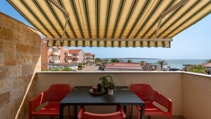 Un balcón con un toldo a rayas, dos sillas rojas, una mesa y una planta en maceta.