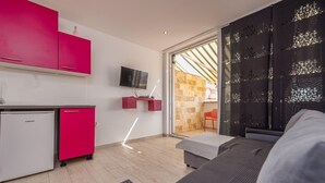 Una habitación de hotel moderna con kitchenette, una cama, un televisor y un ventanal corredero a un espacio exterior.