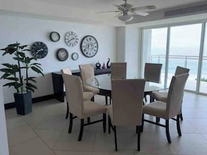 Enjoy meals in this dining area with a large table and six chairs, surrounded by wall clocks and a potted plant.