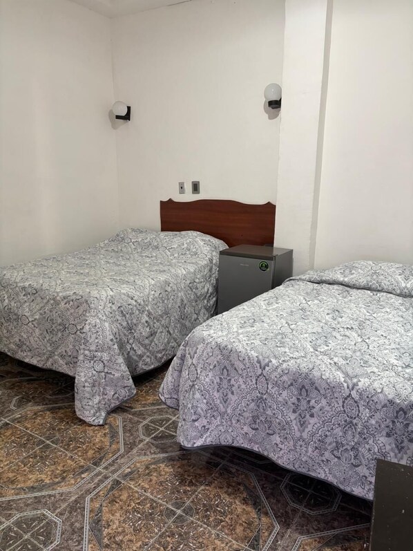 A small, clean room with two beds, a wooden headboard, and a small table. - Habitaciones Climar (Veracruz)