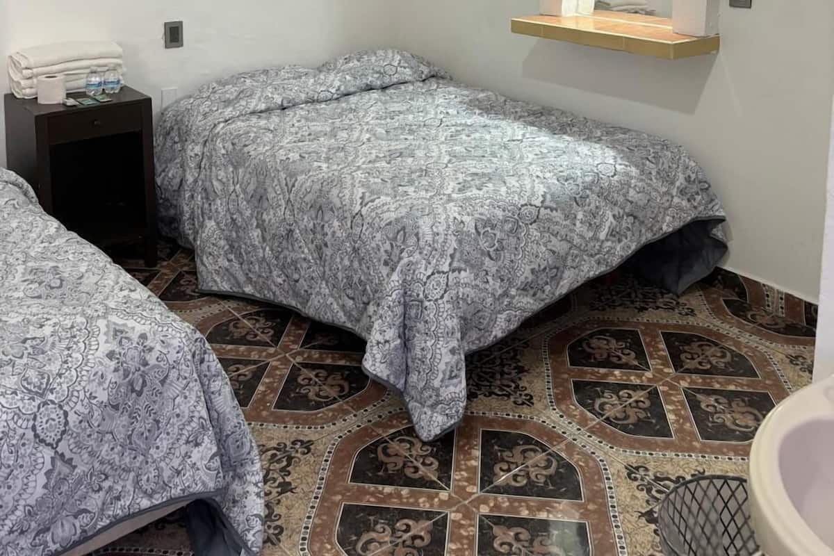 A small, clean room with two beds, a nightstand, a mirror, and a toilet.