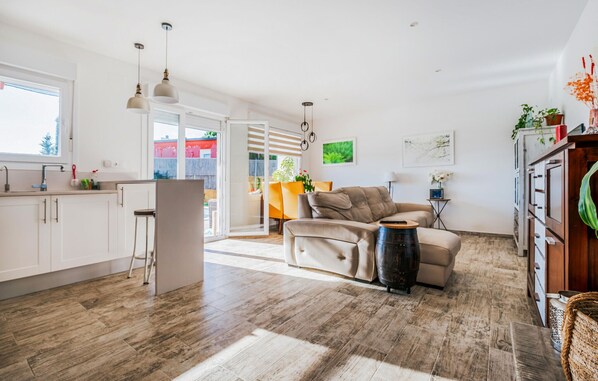 A spacious living area with a sofa, a coffee table, and a dining table with chairs. There is a kitchen area with cabinets and a window. - Lovely home in Tordera (Tordera)