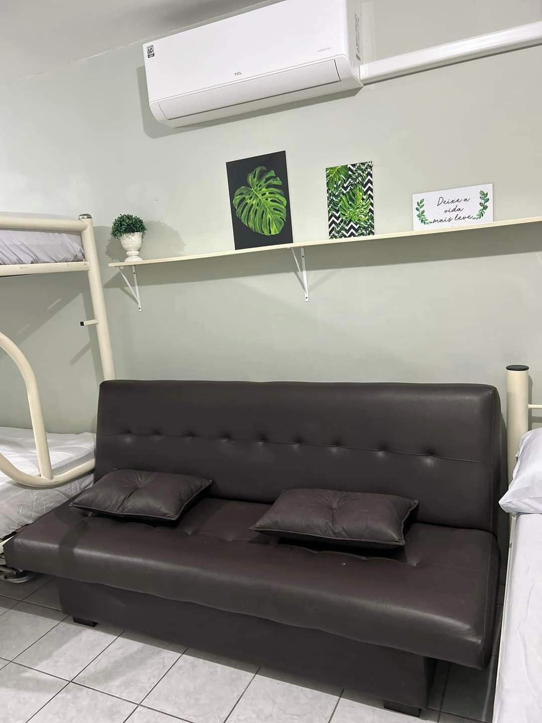 Quarto moderno com sofá marrom escuro, ar condicionado branco e prateleira na parede com objetos decorativos.