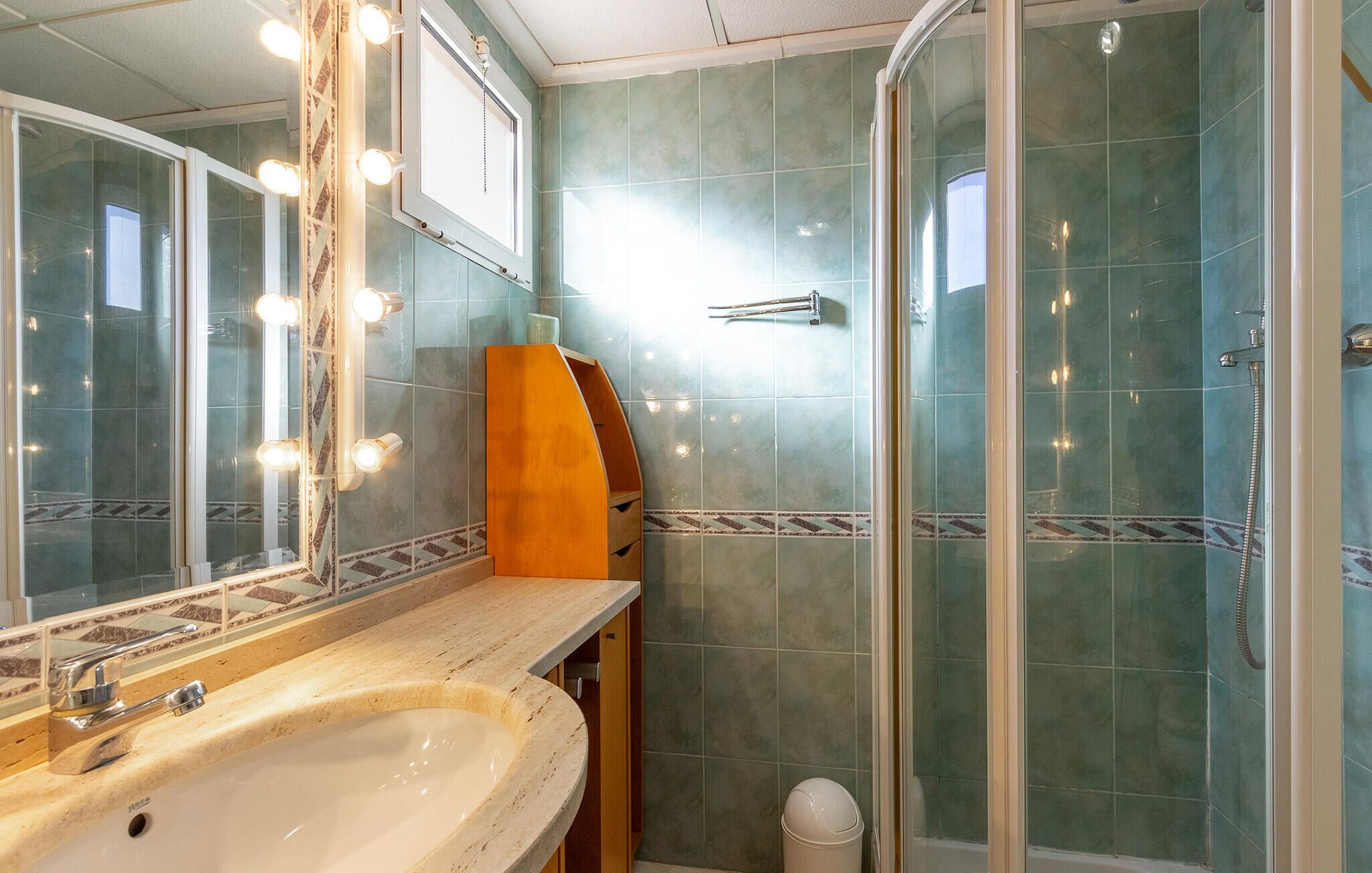 Un baño con lavamanos, espejo, tocador y zona de ducha.