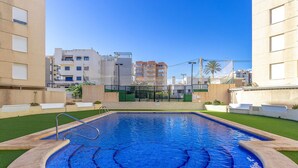 A swimming pool with a clear blue center, surrounded by green artificial grass and beige walls. - Pet friendly apartment in El Campello (El Campello)