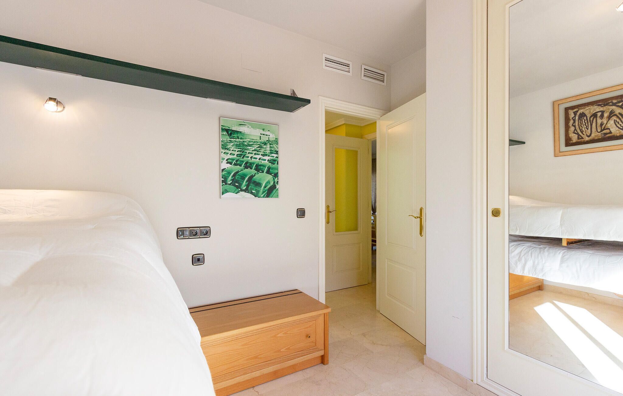 A hotel room with two beds, a wooden bench, a green poster on the wall, and a door leading to another room.