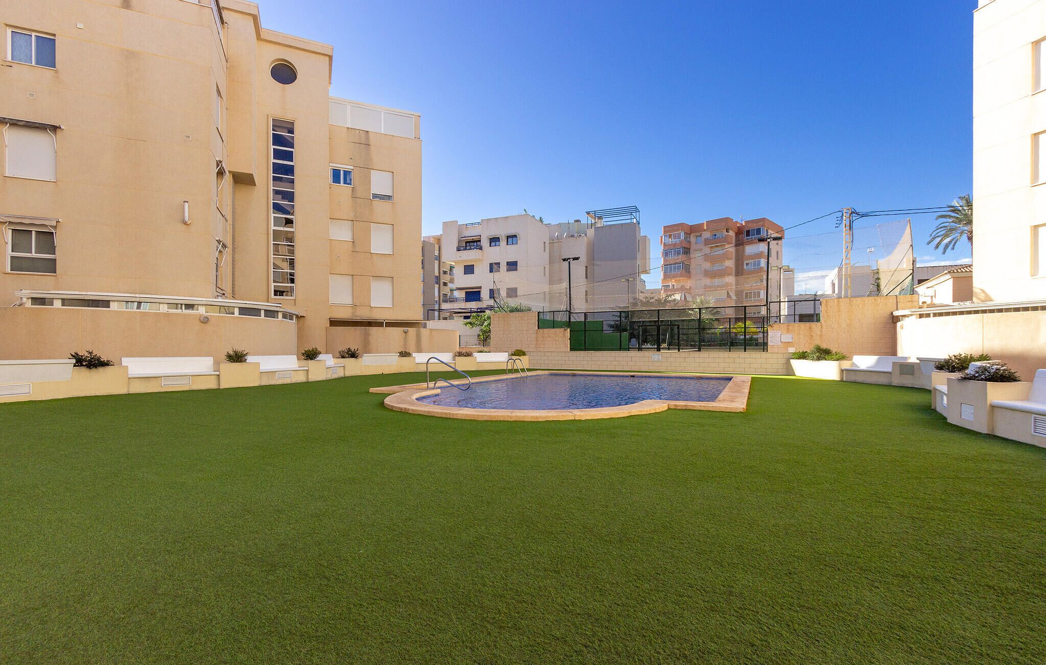 A courtyard with a swimming pool, green lawn, and white outdoor seating.